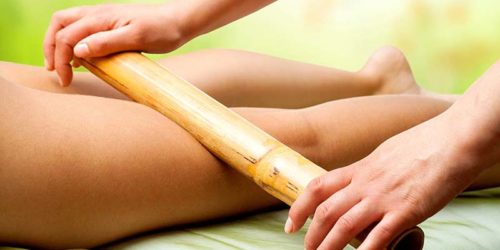 Close up of therapist hands massaging female legs with bamboo stick.